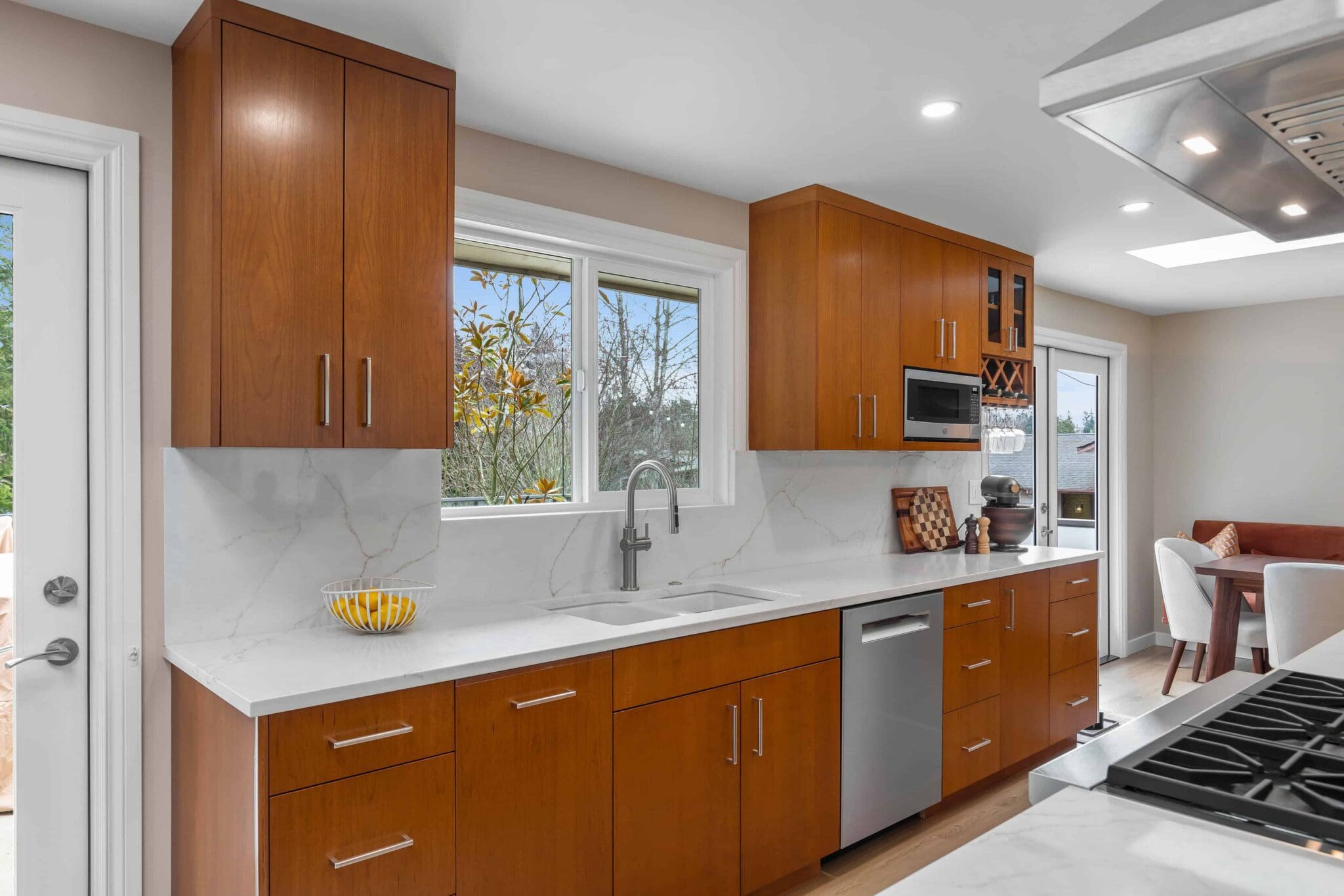 11114-34th-Pl-SW-Seattle-WA_0008-scaled Modern Black Walnut Kitchen with wooden cabinets, white marble countertops and backsplash, stainless steel appliances, a bowl of lemons, and a window above the sink. Dining area visible in the background.