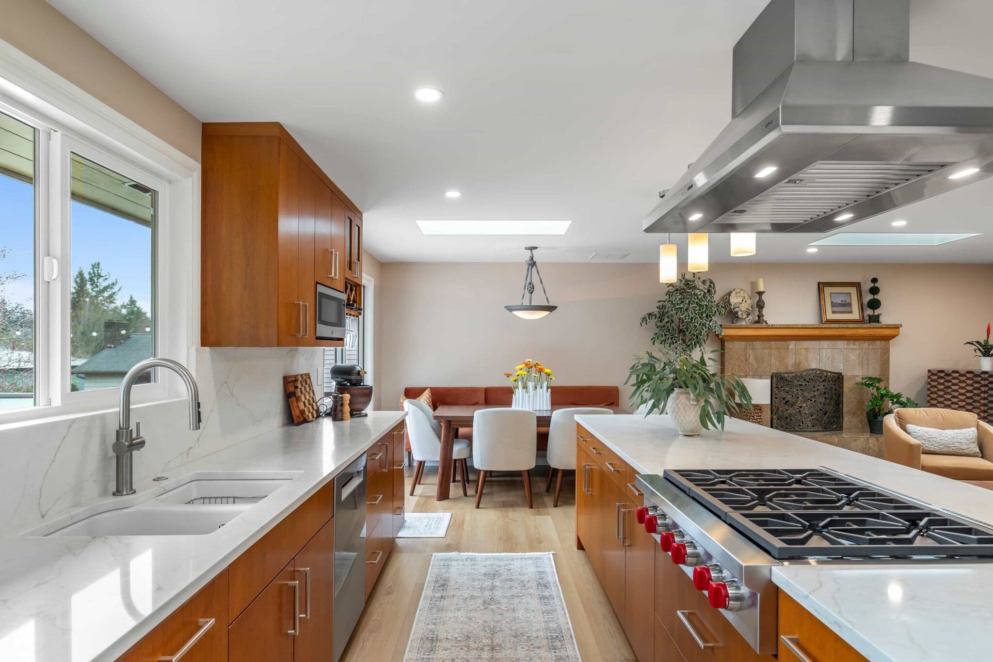 11114-34th-Pl-SW-Seattle-WA_0009-scaled Modern Black Walnut Kitchen with wood cabinets, marble countertops, stainless steel appliances, gas stove, and a view into a dining area and cozy living room with fireplace and plants.