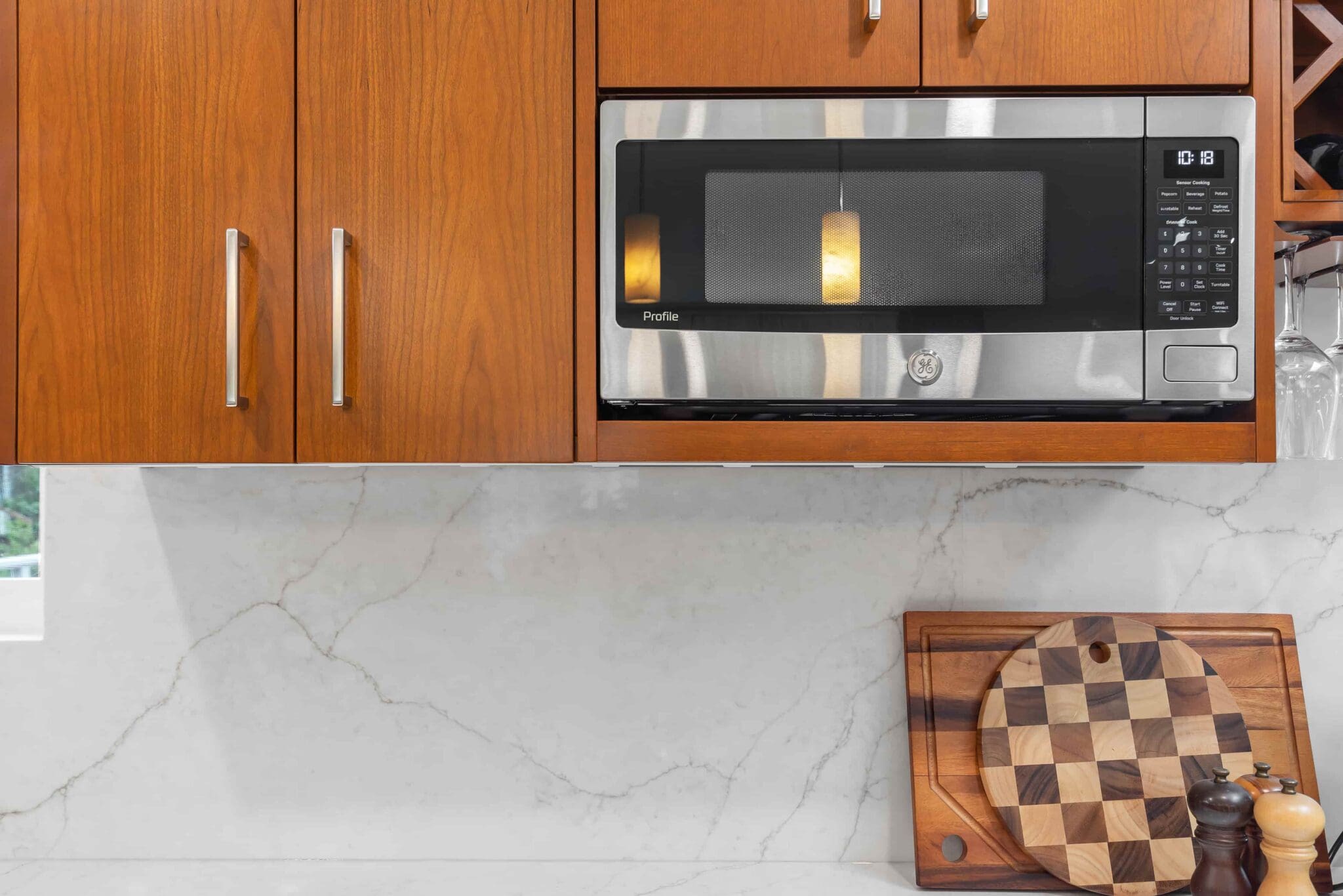 11114-34th-Pl-SW-Seattle-WA_0013-scaled A modern Black Walnut Kitchen with wooden cabinets, a stainless steel microwave, a white marble backsplash, and a checkered cutting board resting on the counter.