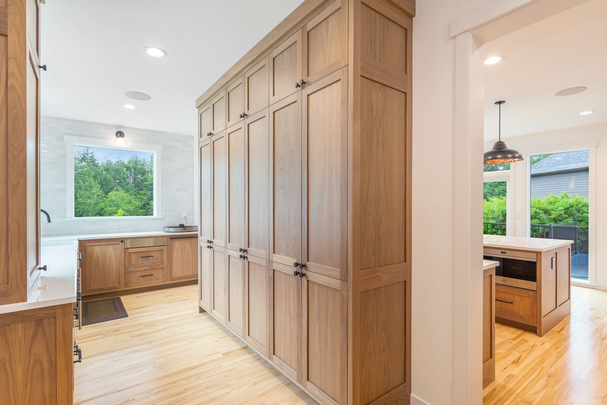 15313-241st-St-SE-Snohomish-WA_0023 Modern cherry kitchen with light wood cabinets, light hardwood floors, and stainless steel appliances. Large windows fill the space with natural light, while a pendant light hangs over the dining area near glass doors.