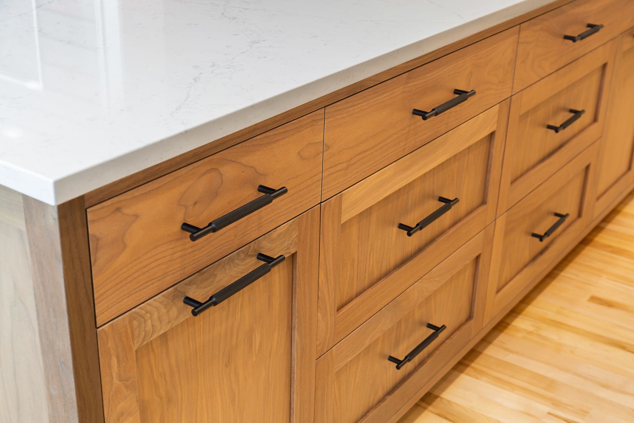 15313-241st-St-SE-Snohomish-WA_0025 Close-up of cherry kitchen cabinets with black handles and a white marble countertop, set on a light-colored wood floor.