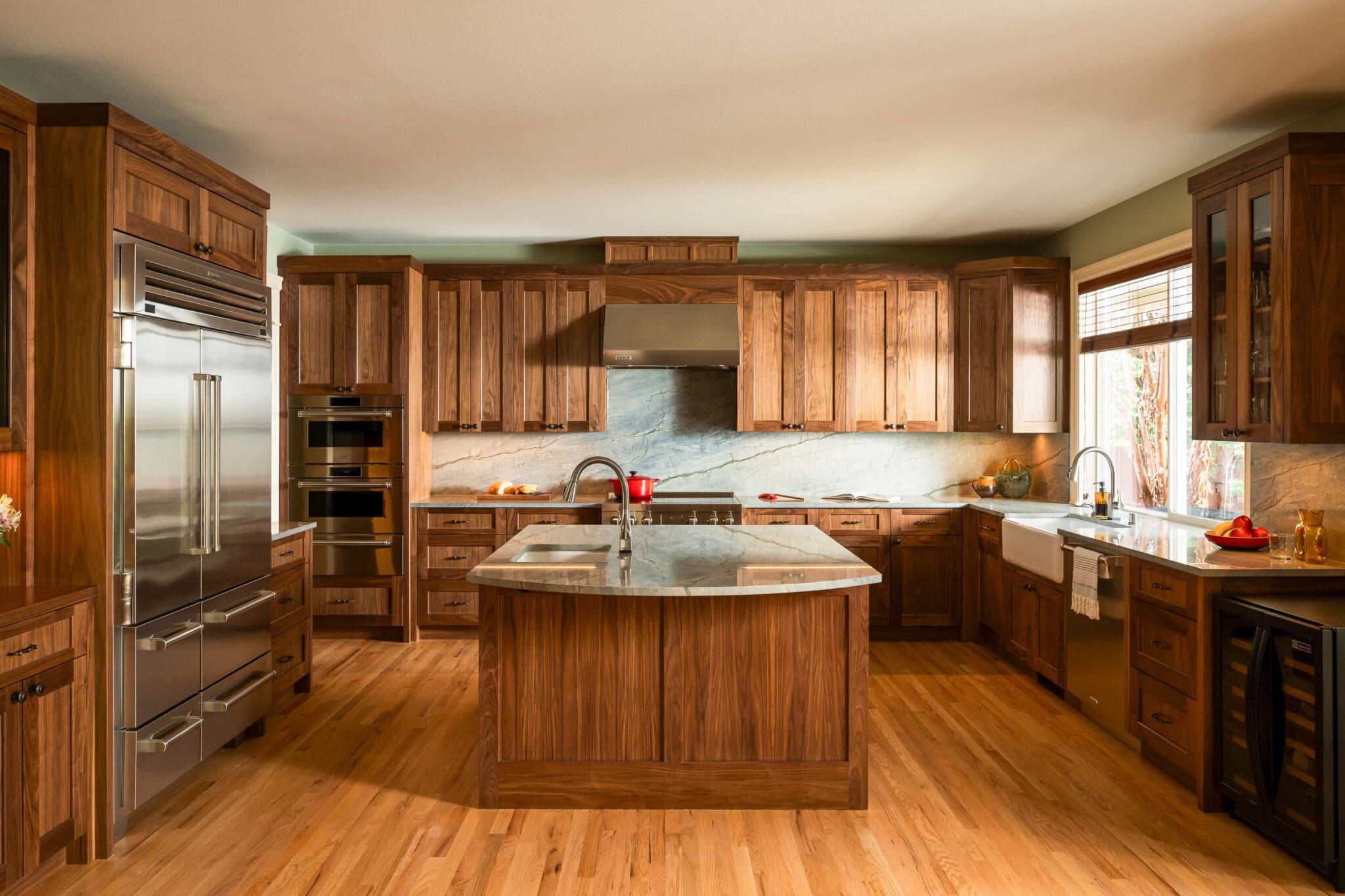 HAAS-Seattle-Kitchen-Remodel-2-2-scaled Spacious kitchen with wooden cabinets, marble countertops, a center island, stainless steel appliances, farmhouse sink, wood floor, and a large window letting in natural light.