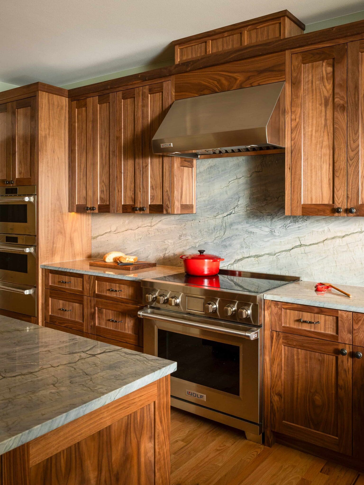 HAAS-Seattle-Kitchen-Remodel-4-2-scaled Modern kitchen with wood cabinets, stainless steel oven and hood, marble countertops and backsplash, and a red pot on the stove. Bread and a knife are on the counter.