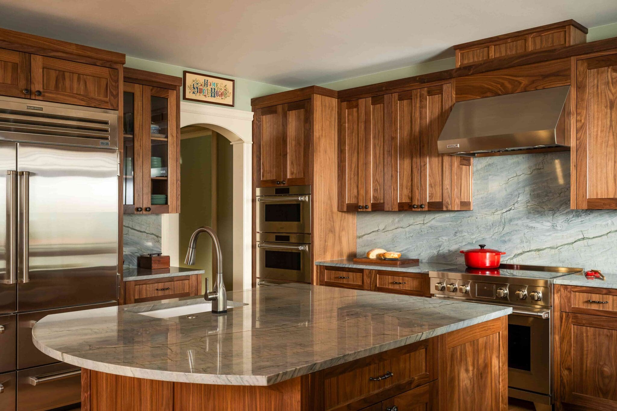 HAAS-Seattle-Kitchen-Remodel-9-2-scaled Modern kitchen with wooden cabinets, stainless steel appliances, marble island with sink, marble backsplash, and a red pot on the stove.