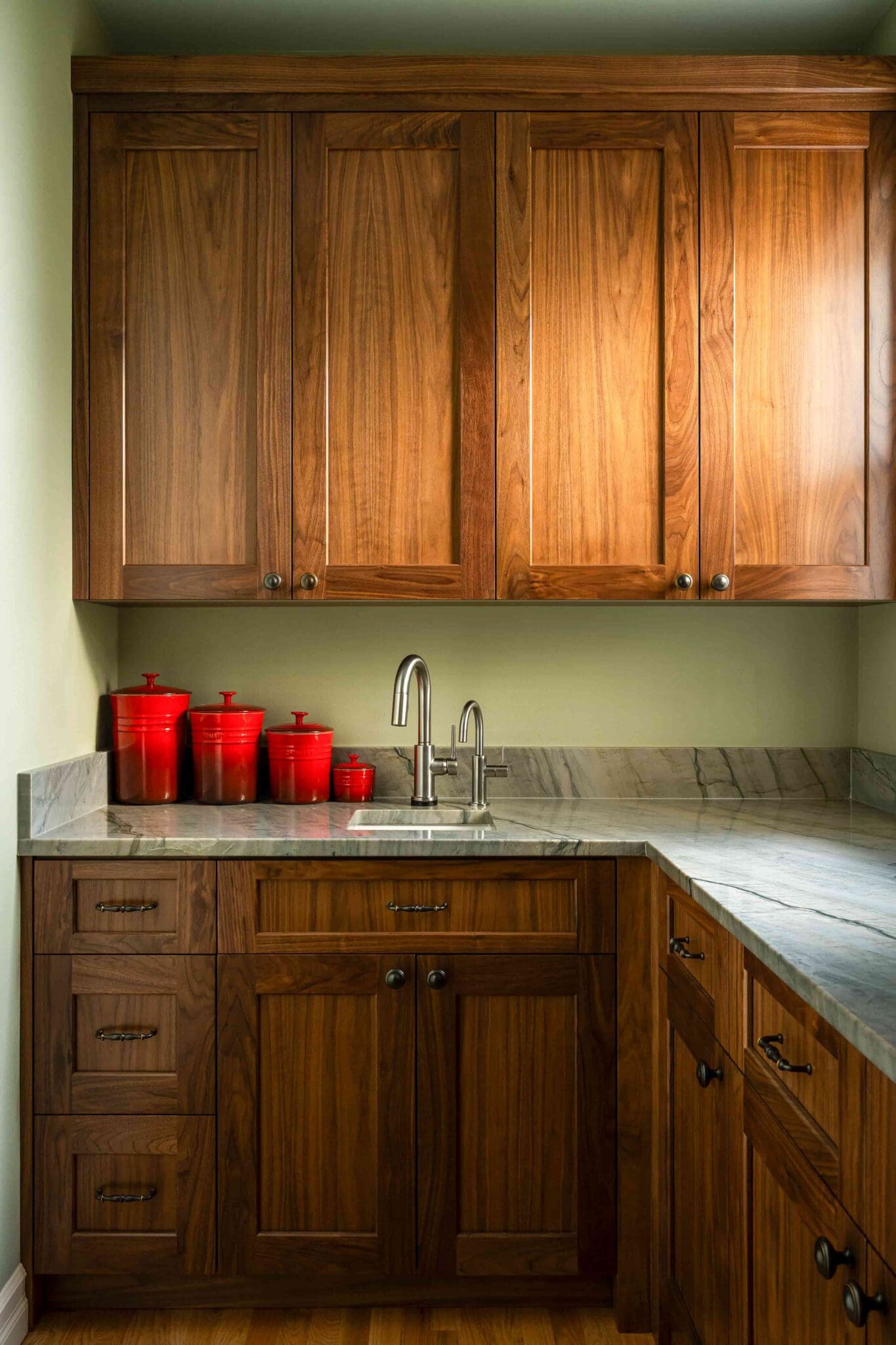 HAAS-Seattle-Pantry-Remodel-11-2-scaled A kitchen with rich wooden cabinets, a marble countertop, a small sink, and four red canisters arranged on the counter in the corner.